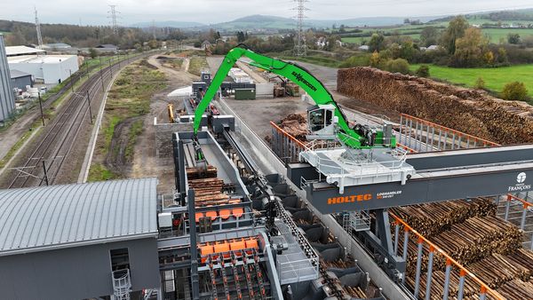 SENNEBOGEN 840 E mit Greifer beim präzisen Einlegen von Rundholz in die HOLTEC-Aufgabeeinheit.