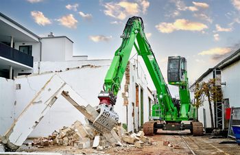 SENNEBOGEN 825 Raupenbagger im Abbrucheinsatz an einem Gebäude mit Sortiergreifer beim Aufnehmen von Mauerwerks- und Betonresten.