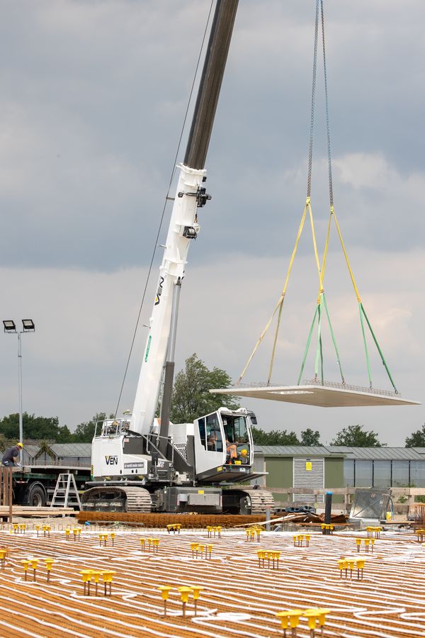 653 Electro Battery Elektrischer SENNEBOGEN 653 Electro Battery hebt eine große Betonplatte über eine bewehrte Baufläche.